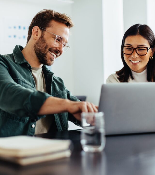 Two colleagues smiling while working on laptop